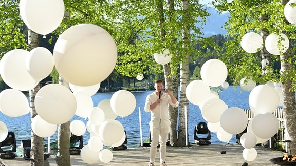 Sänger Ramon Roselly steht auf der Bühne am Ufer eines Sees mit Ballons im Hintergrund