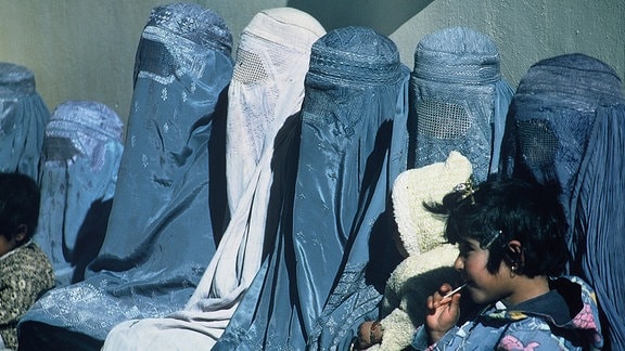 Mehrere afghanische Frauen - alle mit einer Burka bekleidet - sitzen mit einem Kind in einer Klinik.
