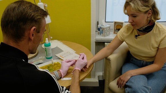 Denis zieht für einen HIV-Test einen Tropfen Blut von MDR-Autorin Marie Landes‘ Finger ab.