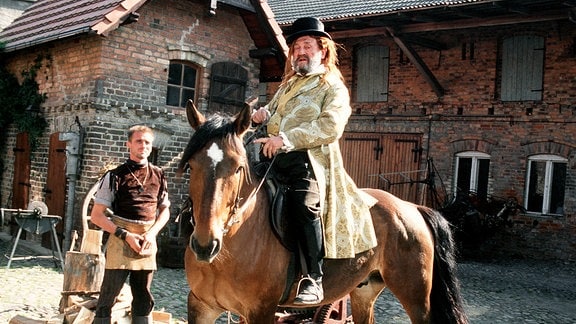 Der verschlagene Kaufmann (Rolf Hoppe) sitzt auf dem hohen Ross. Wieder einmal hat er ein gutes Geschäft gemacht.