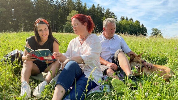 Clarissa, Dana und Heiko sitzen im Gras.