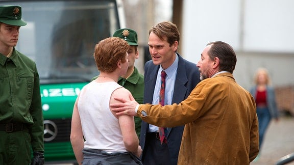 Peter Simon (Fabian Hinrichs, M.) versucht Reiko Böttcher (Leon Seidel, l.) zu konfrontieren. Hajo Gärster (Thorsten Merten, r.) kommt seinem Neffen jedoch zu Hilfe. (mit Komparsen im HG.)