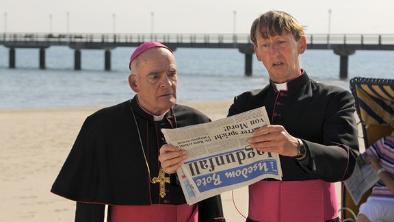 Bischof Hemmelrath (Hans-Michael Rehberg, li.) und Monsignore Mühlich (Gilbert von Sohlern) erfahren aus der Zeitung, dass Pfarrer Braun wieder "kriminalisiert" hat.