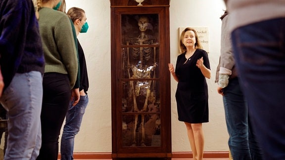 Prof. Dr. Heike Kielstein, Anatomin der Universitätsmedizin Halle, steht neben einem menschlichen Skelett und spricht zu mehreren Zuhörern.