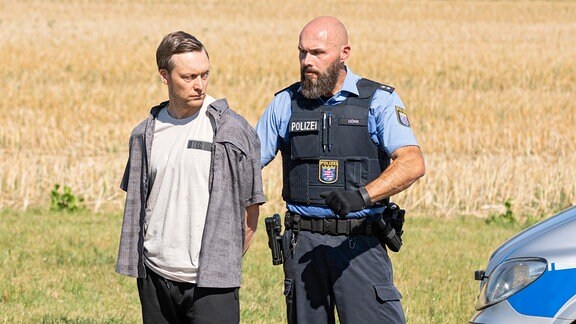 Stephan Ernst (Robin Sondermann, links) wird von einem Polizeibeamten an den Tatort geführt.