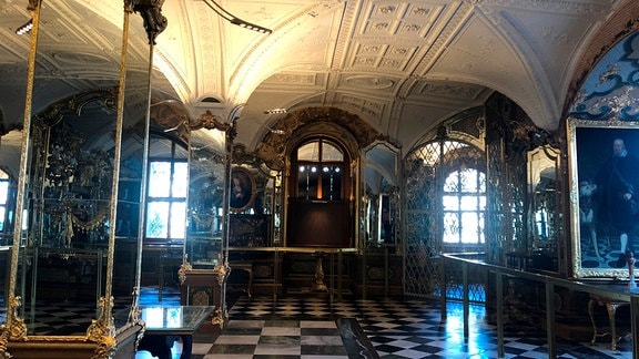Ein barockes Prachtkabinett mit großen Porträt-Gemälden, goldenen Vitrinen mit Schmuckstücken, Marmorbodenplatten und Stuck.