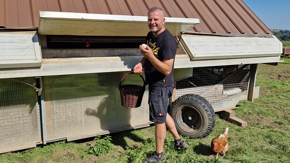 Ein Mann sammelt Eier aus einem Hühnermobil