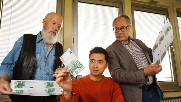 Die Rentnercops Reinhard Bielefelder (Bill Mockridge, l.) und Klaus Schmitz (Hartmut Volle, r.) versuchen sich als Geldfälscher. Hui Ko (Aaron Le, M.) begutachtet das Ergebnis.