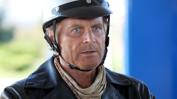 Thomas (Terence Hill) hält mit seinem Motorrad an einer Tankstelle.