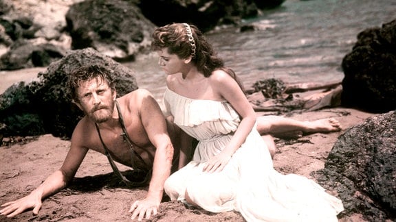 Odysseus (Kirk Douglas) erwacht an einem Strand. Neben ihm sitzt Prinzessin Nausikaa (Rossana Podestà). 