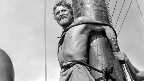 Odysseus (Kirk Douglas) steht gefesselt an Deck eines Schiffes. 