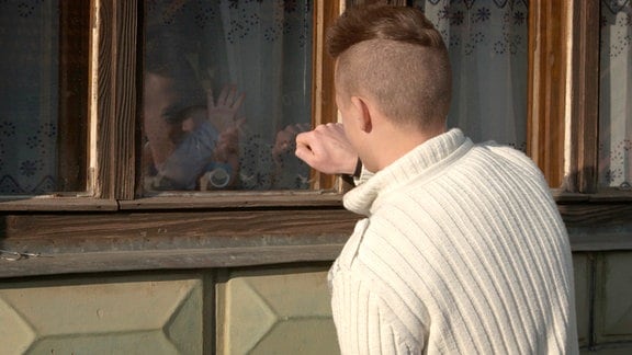 Haris blickt ein  Baby hinter einem Fenster an. 