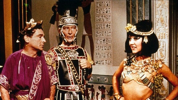 Julius Cäsar (Kenneth Williams, Mitte) mit seinem Leibwächter Hengist (Kenneth Connor, r.) zu Besuch bei Kleopatra (Amanda Barrie).