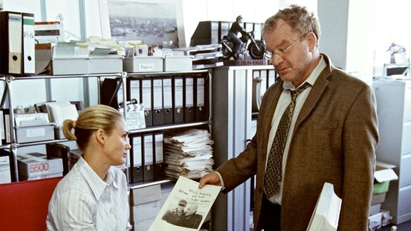 Eine Frau und ein Mann in einem Büro. Der Mann zeigt seiner Kollegin eine Schwarz-Weiß-Aufnahme.