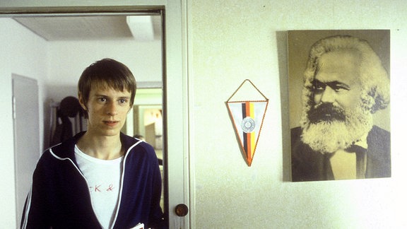 Micha (Alexander Scheer) steht in einer geöffneten Tür. An detr Wand ein  Karl-Marx-Poster.