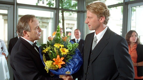 Der Verwaltungsratsvorsitzende Hansen (Dieter Bellmann) übergibt dem Chirurgen Dr. Michael Mangold (Michael von Au) augfrund der Beförderung zum Chefarzt einen Blumenstrauß.