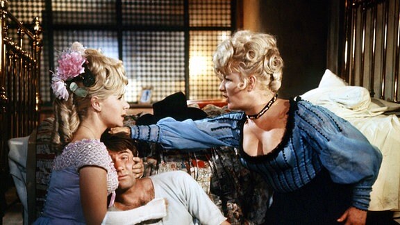 Annie (Angela Douglas, l.) und Belle (Joan Sims), die Saloonbesitzerin, streiten sich um den angeblichen Marshal (Jim Dale). 