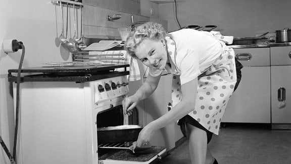 Eine Frau nimmt einene Backform aus dem Küchenherd.