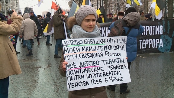 Kamilla trägt das Textplakat auf einer Protestdemonstration mit folgendem Inhalt: "Die Kindheit meiner Oma: Tauwetter. Die Kindheit meiner Mama: Perestrojka, freies Russland. Meine Kindheit: Terrorakte, politische Morde."