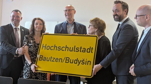 Männer halten ein Ortsschild "Hochschulstadt Bautzen/Budyšin"