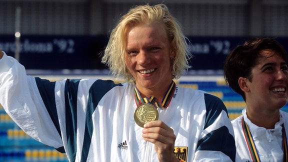 Dagmar Hase freut sich und zeigt ihre Medaille als Olympiasiegerin 1992.