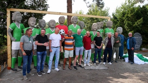 Eine Personengruppe posiert in einer Reihe vor Statuen.