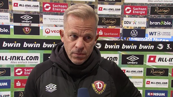 Dynamo-Trainer Markus Anfang vor einer Werbetafel im MDR-Interview