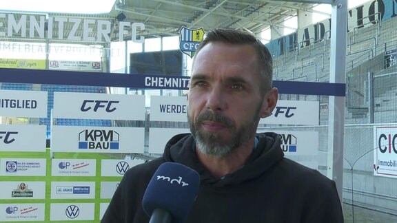 Chemnitz-Trainer Christian Tiffert vor einer Werbebande im Stadion am Mikrofon
