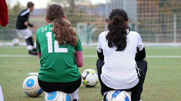 Zwei Mädchen auf einem Sportplatz sitzen auf einem Ball.
