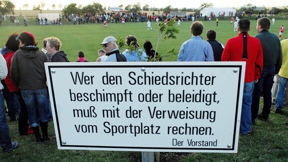 Schild am Spielfeldrand mit der Aufschrift "Wer den Schiedsrichter beschimpft und beleidigt, muß mit dem Verweis vom Sportplatz rechnen".
