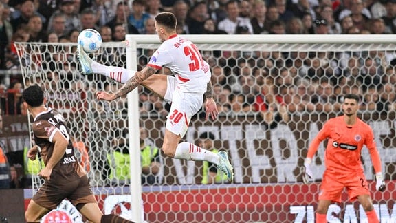 Benjamin Sesko (Leipzig 30) versucht mit Willi Orban (Leipzig 04) ein Tor vorbei an Torhueter Nikola Vasilj (Pauli 22) zu schiessen.