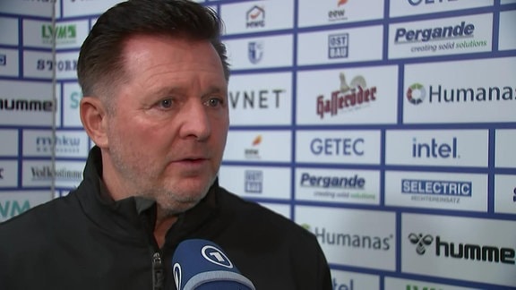 Trainer im Interview vor Werbebande