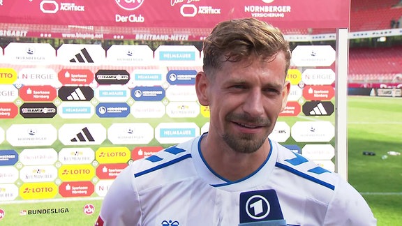 Spieler im Interview vor Werbebande grinsend