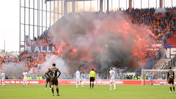Fans von Hansa Rostock zünden Bengalos in blau-weissen Vereinsfarben.