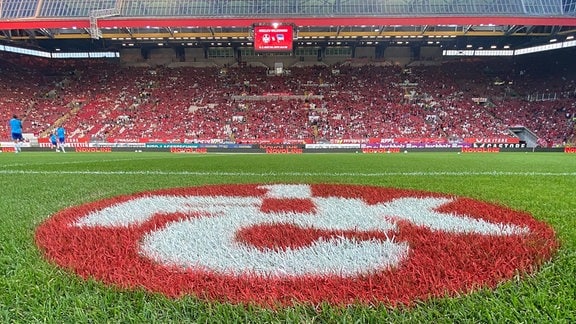 In einem Fußballstadion ist das Wappen des 1. FC Kaiserslautern auf dem Rasen.