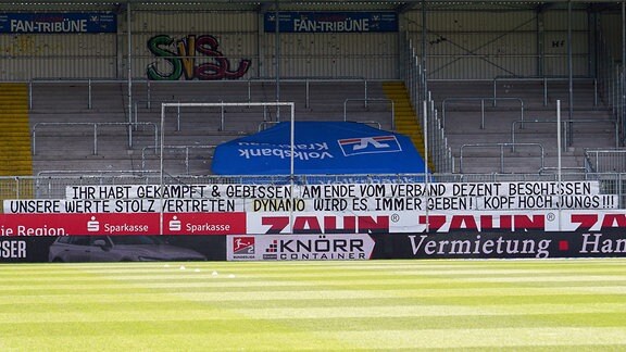 er leere Gästefanblock von SG Dynamo Dresden zeigt einen Banner mit der Aufschrift: Ihr habt gekämpft und gebissen. Am Ende vom Verband dezent beschissen. Unsere Werte stolz vertreten. Dynamo wird es immer geben. Kopf hoch, Jungs