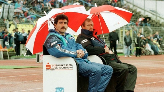 Co-Trainer Damian Halata (li.) und Cheftrainer Sigi Held sitzen am 29.09.1996 im Bruno-Plache Stadionunter Regenschirmen