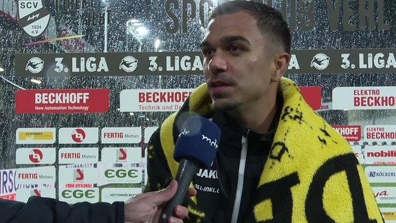 Spieler im Regen im Interview vor Werbebande