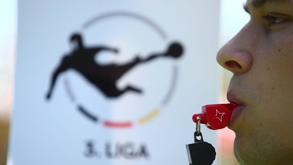 Schiedsrichter pfeift vor dem Logo der 3. Liga.