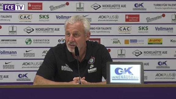 Aue-Trainer Pavel Dotchev auf einer Pressekonferenz vor einer Werbetafel am Mikrofon