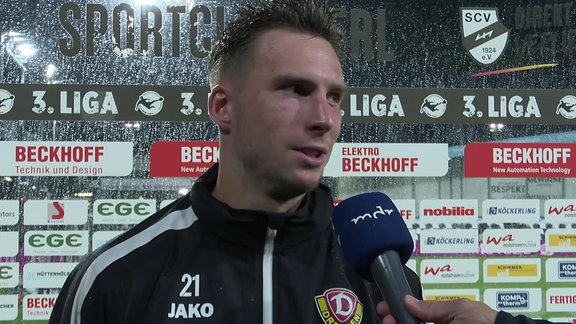 Spieler im Regen im Interview vor Werbebande