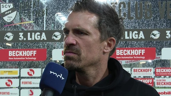 Trainer im Interview im Regen vor Werbebande