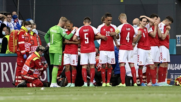 Die Fussballer der dänischen Nationalmannschaft bilden einen Kreis um Christian Eriksen, der medizinisch behandelt wird.