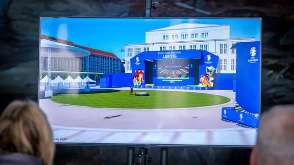 Interessierte betrachten einen Bildschirm, der ein 3D-Modell einer zukünftigen "Fan Zone" für die Fußball Europameisterschaft der Herren am Augustusplatz in Leipzig.