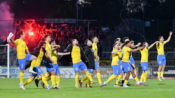 Mannschaft des 1. FC Lokomotive Leipzig feiert den Sieg. Bengalos im Block der Fans des 1. FC Lokomotive Leipzig im Hintergrund.