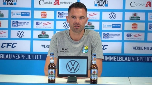 CFC-Trainer vor Werbebande auf einer Pressekonferenz