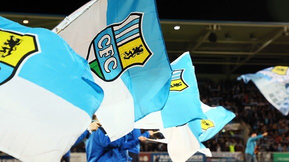 Fahnen mit dem Logo des Chemnitzer FC werden im Stadion geschwenkt.