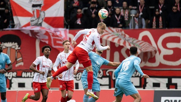 Ben-Luca Moritz ( 2; FC Rot-Weiß Erfurt) steht während eines Kopfballs in der Luft, während ihn umgebende Mitspieler zuschauen.