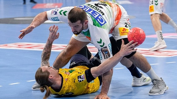Intensiver Zweikampf in einem Handballspiel bei dem ein Spieler auf dem Boden liegt.