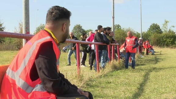 Ordner sitzt bei einem Fußballspiel am Rand des Spielfeldes und beobachtet die Fans auf einem kleinen Platz im Amateurfußball